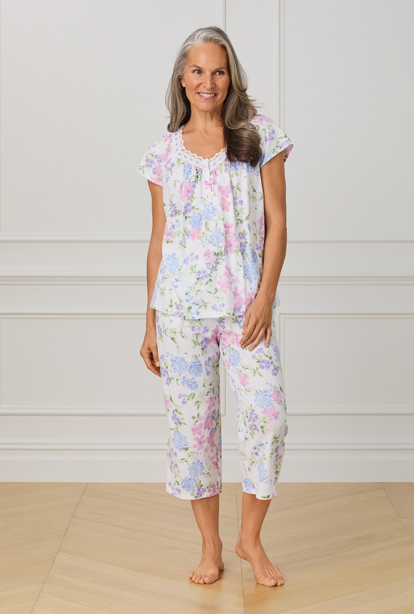 A lady wearing multi color cap sleeve capri pant pajama set with lilac and periwinckle garden print.