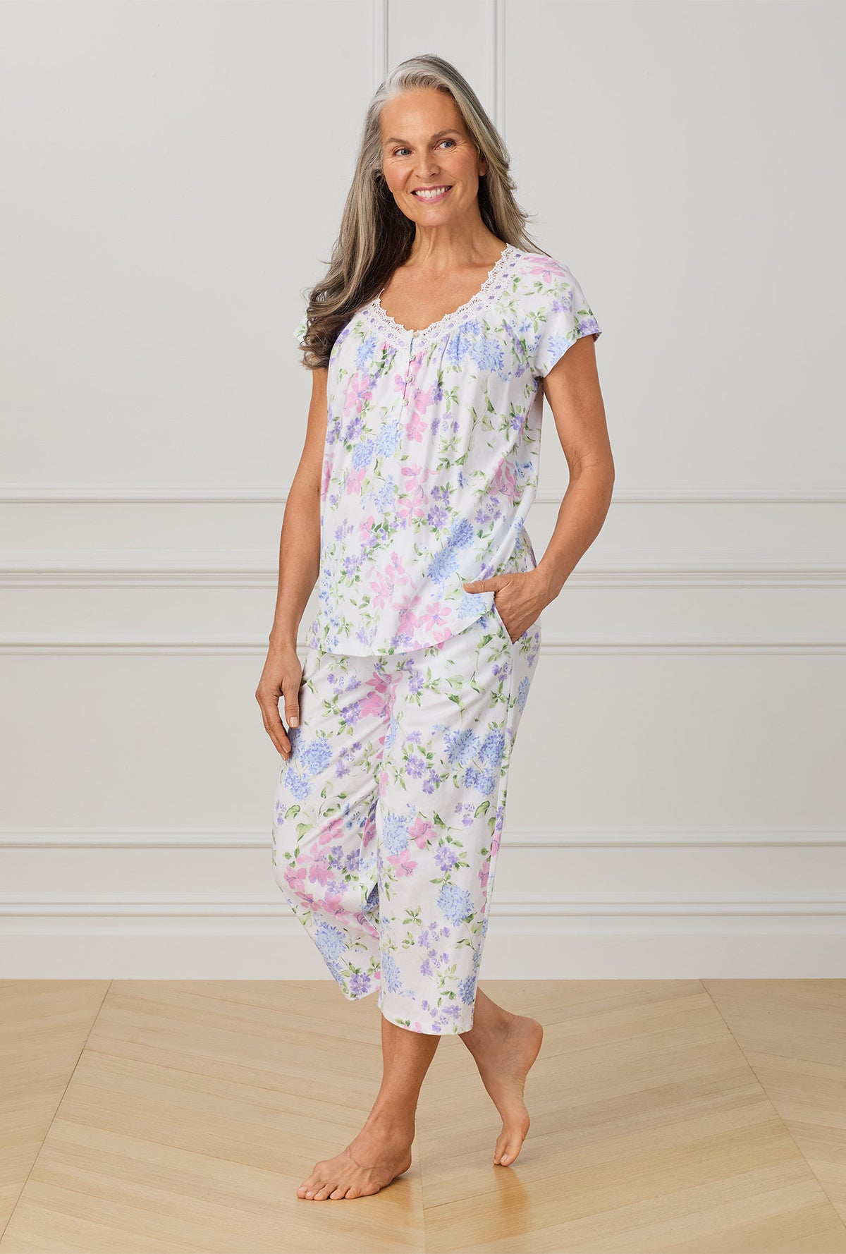 A lady wearing multi color cap sleeve capri pant pajama set with lilac and periwinckle garden print.