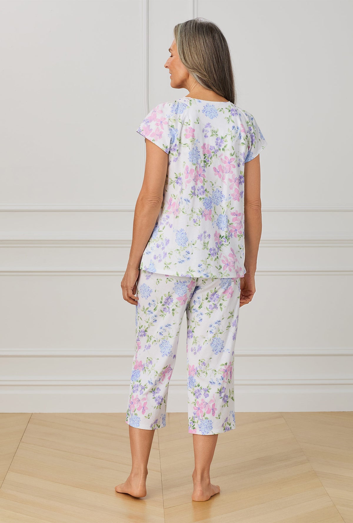 A lady wearing multi color cap sleeve capri pant pajama set with lilac and periwinckle garden print.